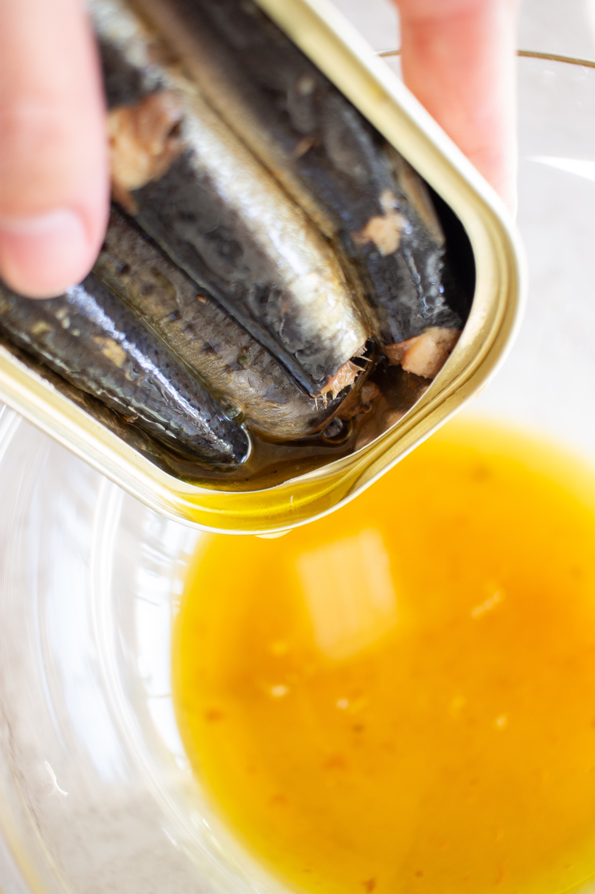 Emptying oil from canned sardines into a bowl.